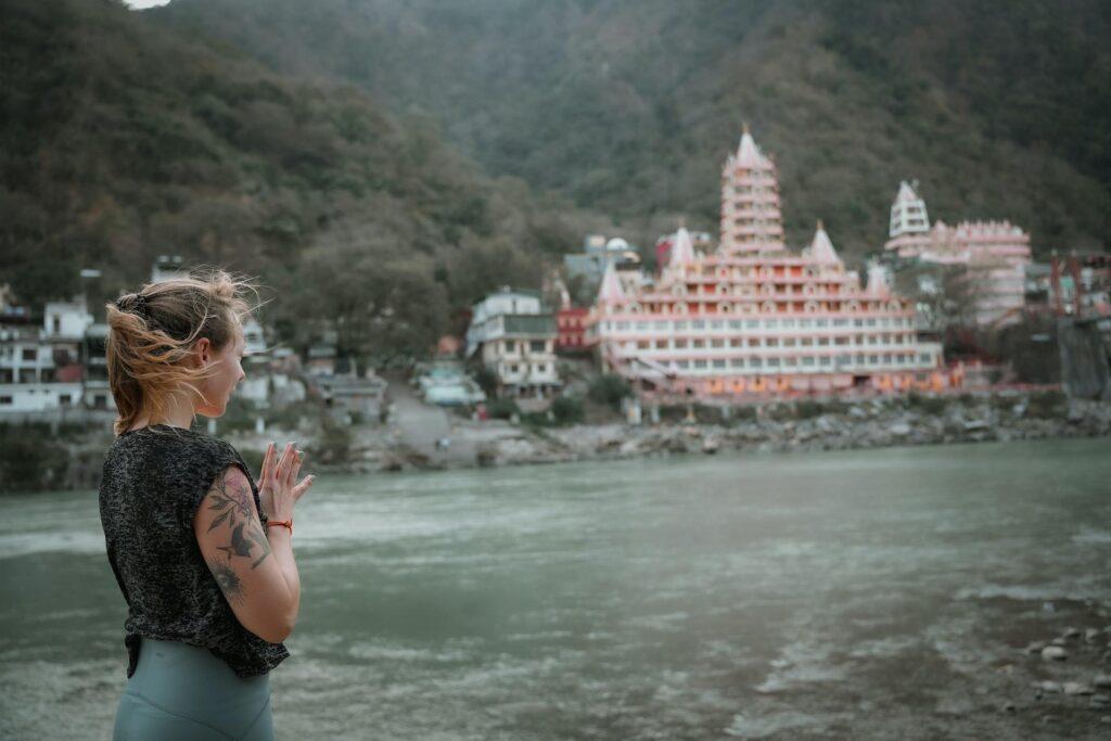 A serene scene along the Ganges River in Rishikesh, showcasing a devotee engaged in prayer rituals. Witness the spiritual essence of Haridwar & Rishikesh on your unforgettable One Day Delhi to Haridwar & Rishikesh Trip.